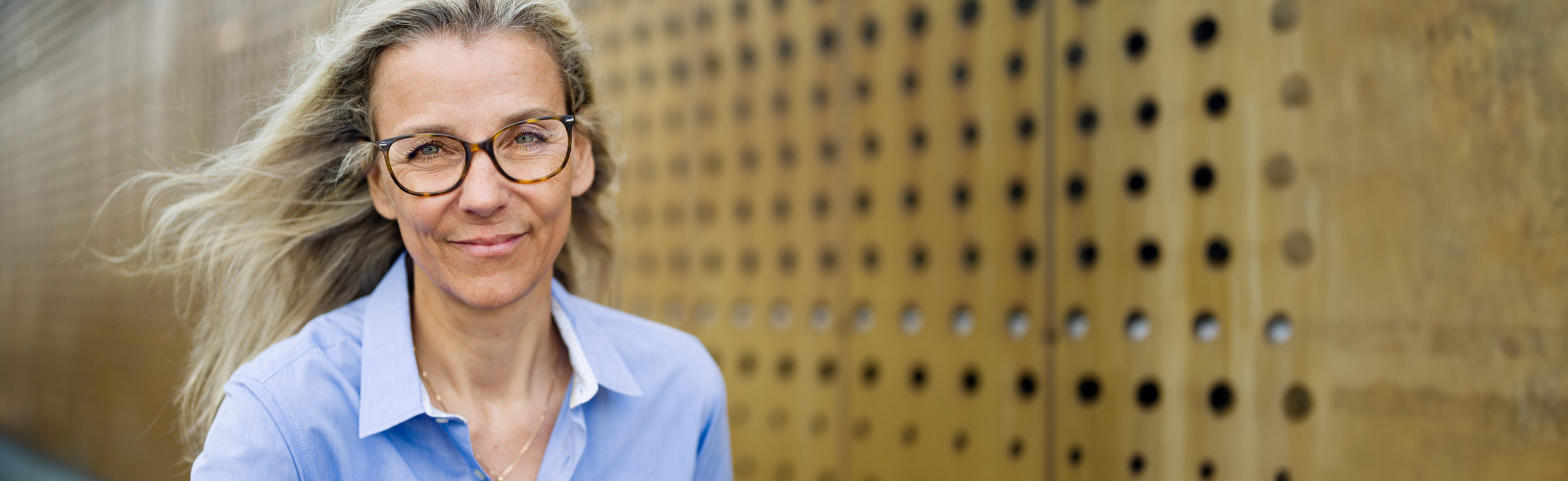 Blau mit Brille laechelnd vor goldener Lochwand